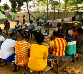 Group of people sitting outside on chairs, under trees in Ethiopia.