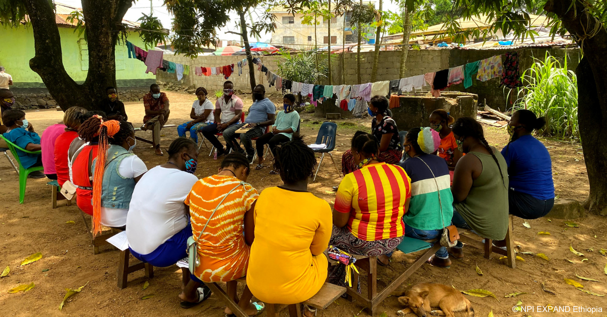 Group of people sitting outside on chairs, under trees in Ethiopia.