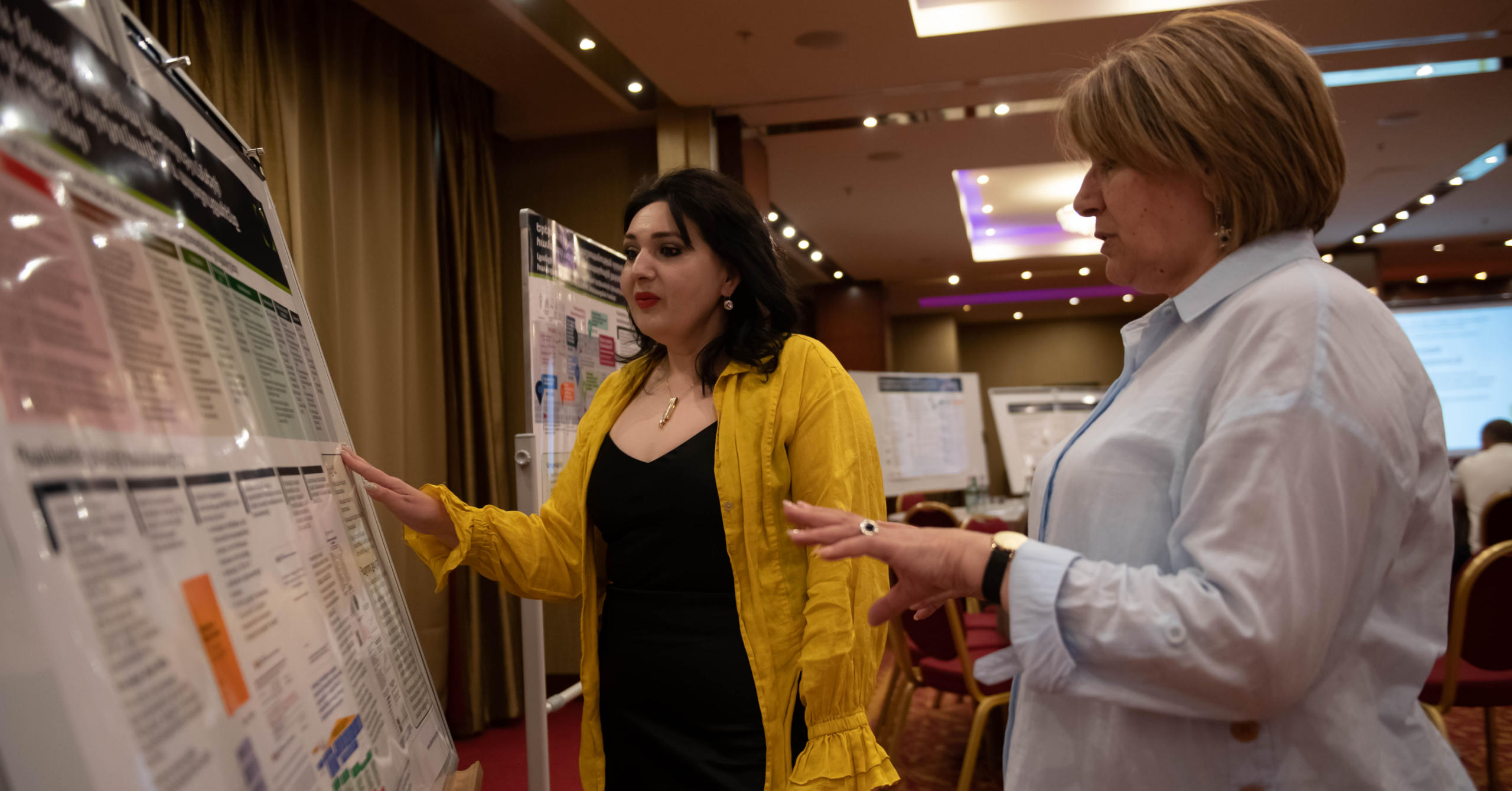 Photo showing attendees at the D4I close out event in Armenia reviewing a poster on D4I’s work in Armenia during the gallery walk.