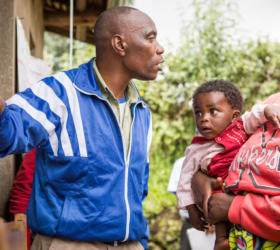 Photo showing a mother and her baby receiving health information from a man pointing to a chart in Rwanda.