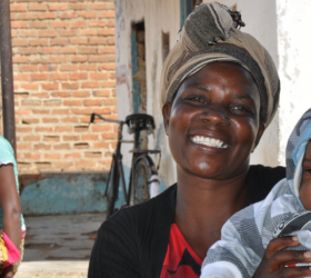Photo of a Zambian woman smiling and holding a baby.